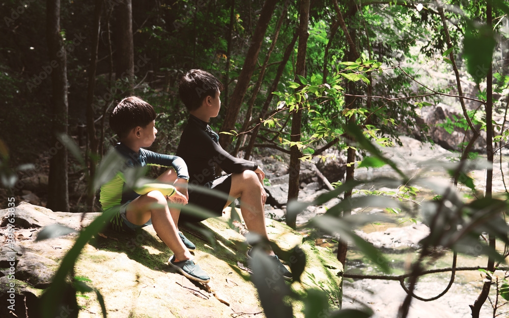 Two brothers boy relaxing sit on the rock by the river fall in the ...