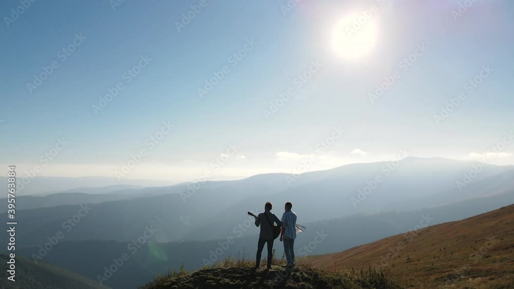 Aerial view silhouette of males enjoying with guitar on their mountains vacation at sunset. Man playing guitar in nature. Musician playing guitar in the mountains during sunset on the sunlight. Aerial view silhouette of males enjoying with guitar on their mountains vacation at sunset. Man playing guitar in nature. Musician playing guitar in the mountains during sunset on the sunlight.