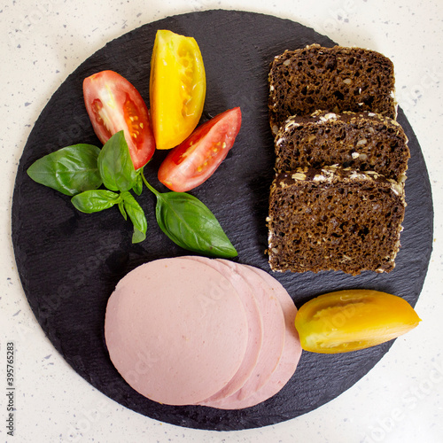 Appetizing sausage, bologne sliced on a slate board on a light marble background with tomatoes, close up, top view photo