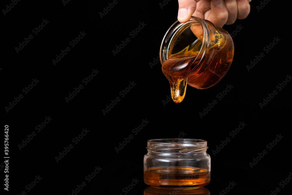 Liquid honey on a black background flows from one jar to another. Liquid honey on a black background flows from one jar to another.