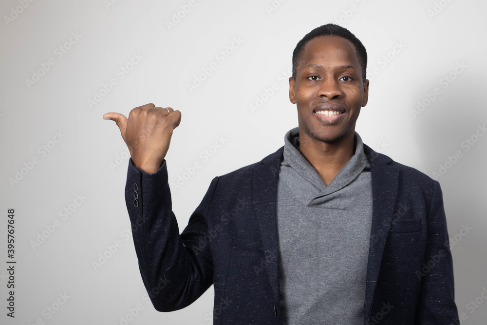Look at this! Handsome young African man pointing up and smiling to you while standing against grey background Look at this! Handsome young African man pointing up and smiling to you while standing against grey background
