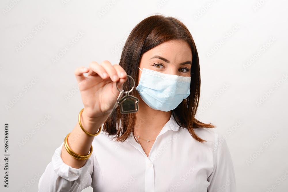 portrait of beautiful young real estate agent business woman wearing surgical mask and holding house keys portrait of beautiful young real estate agent business woman wearing surgical mask and holding house keys