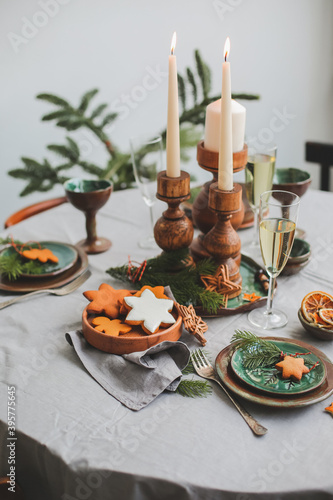 Festive Christmas and New Year table setting in scandinavian style with rustic handmade details in natural and white tones. Dining place decorated with pine cones, branches and candles