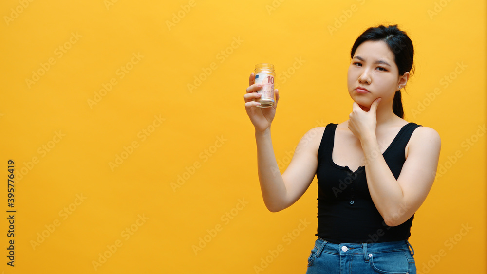 Sad pensive young asian woman holding money jar with savings. Low income and big expenditure concept. High quality photo Sad pensive young asian woman holding money jar with savings. Low income and big expenditure concept. High quality photo