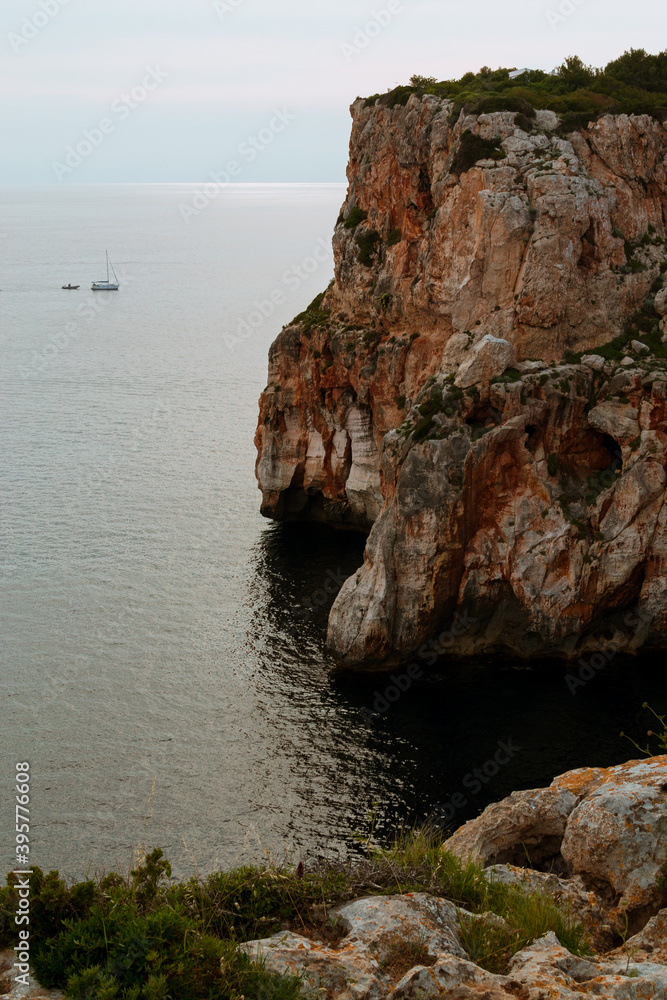 Cliff over mediterranean sea and a boat in the distance.