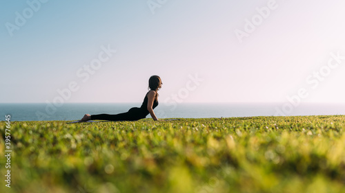 Profesora de yoga concentrada viste de negro practica yoga recostada en el césped al aire libre disfrutando de la tarde.