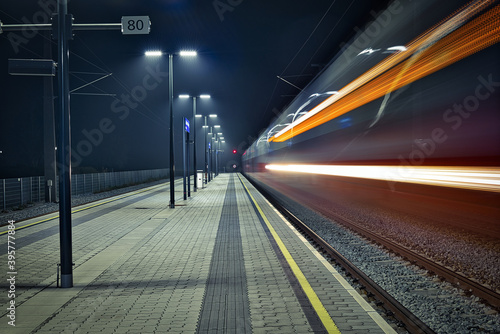 Aufnahme eines menschenleeren hell erleuchteten Bahnsteiges in den Abendstunden während ein Zug vorbeifährt photo