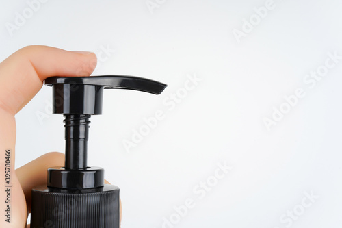 Hand pushing black pump dispenser, white background. Sanitizer, cosmetology, beauty, washing hands concept. Close-up, copy space