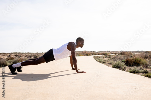 Young black runner in profile doing push-ups.