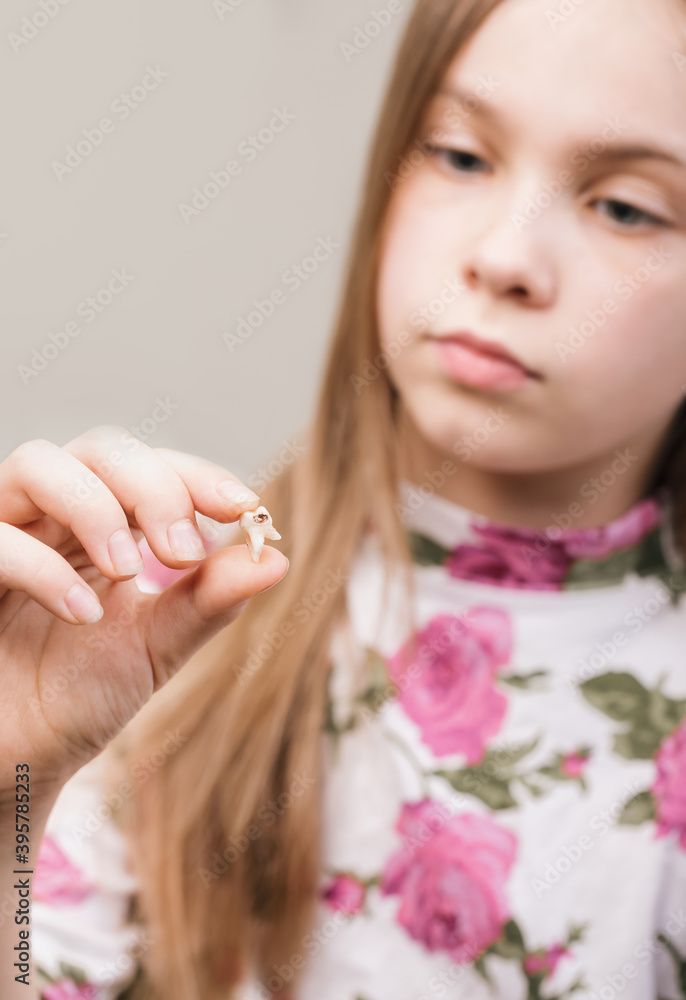 Girl looking at extracted milk tooth with caries - bad oral hygiene concept