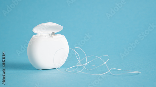 Container with dental floss. Floss on blue background. White dental floss case isolated. Open dental floss container