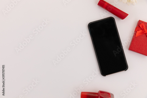 Smartphone, red lipstick, nail varnish, present and flowers on white background