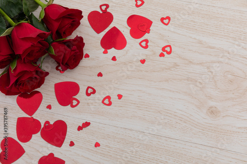 Bunch of red roses and red hearts lying on wooden background