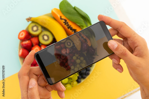 Woman taking photos with smartphone of bowl of fruit