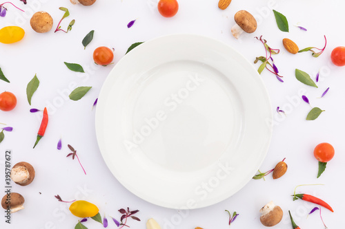 White plate surrounded by fresh vegetables on white background