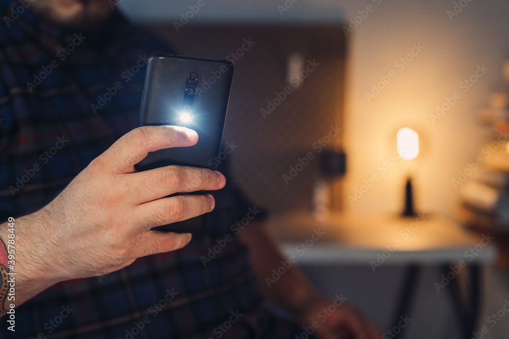 Closeup shot of a man's hand taking a picture with a turned on mobile phone camera flashlight - obrazy, fototapety, plakaty 