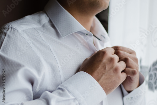 man in white shirt, groom buttons up his shirt