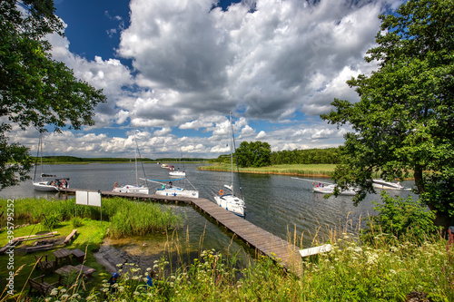 Fototapeta Naklejka Na Ścianę i Meble -  Krajobraz wodny. Molo na jeziorze i białe żaglówki. Wakacje nad jeziorem. 