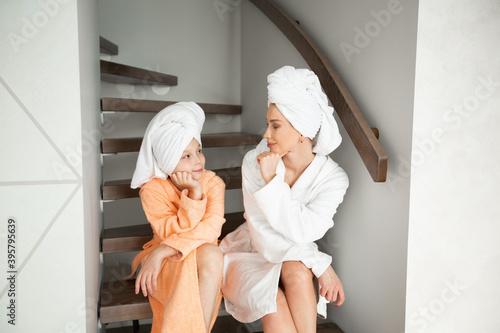 Obraz na płótnie beautiful mom with daughter in bathrobes sitting on the stairs at home