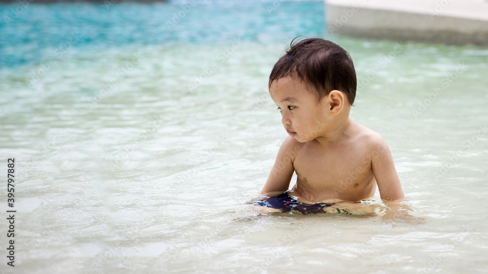 Asian boy toddler sitting in the water in swimming pool inside resort hotel. Thinking face expression. Asian boy toddler sitting in the water in swimming pool inside resort hotel. Thinking face expression.
