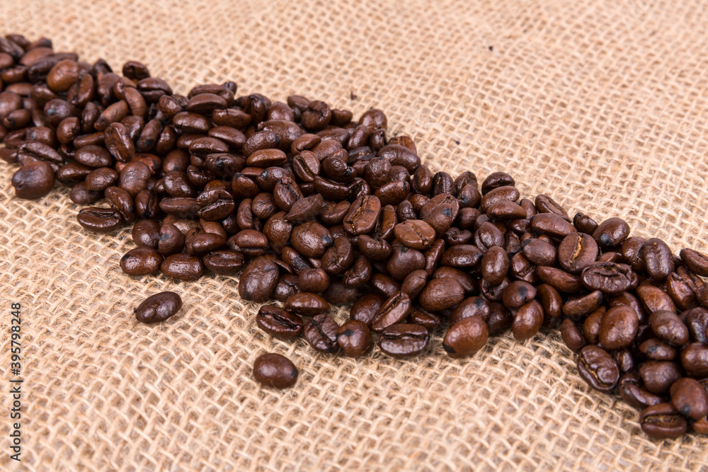 Fototapeta premium Diagonal line of roasted brown coffee beans over a burlap textured cloth