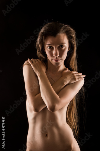 Portrait of a Nude young woman with long hair in contrast lighting on a dark background.