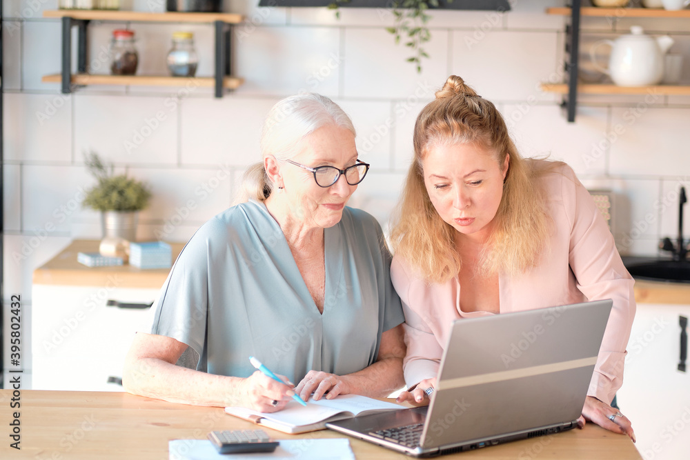 daughter helps her elderly mother figure it out online with her personal account. Woman teaching senior mother to use internet at home. Senior woman with her daughter looking at modern gadget indoors. daughter helps her elderly mother figure it out online with her personal account. Woman teaching senior mother to use internet at home. Senior woman with her daughter looking at modern gadget indoors.