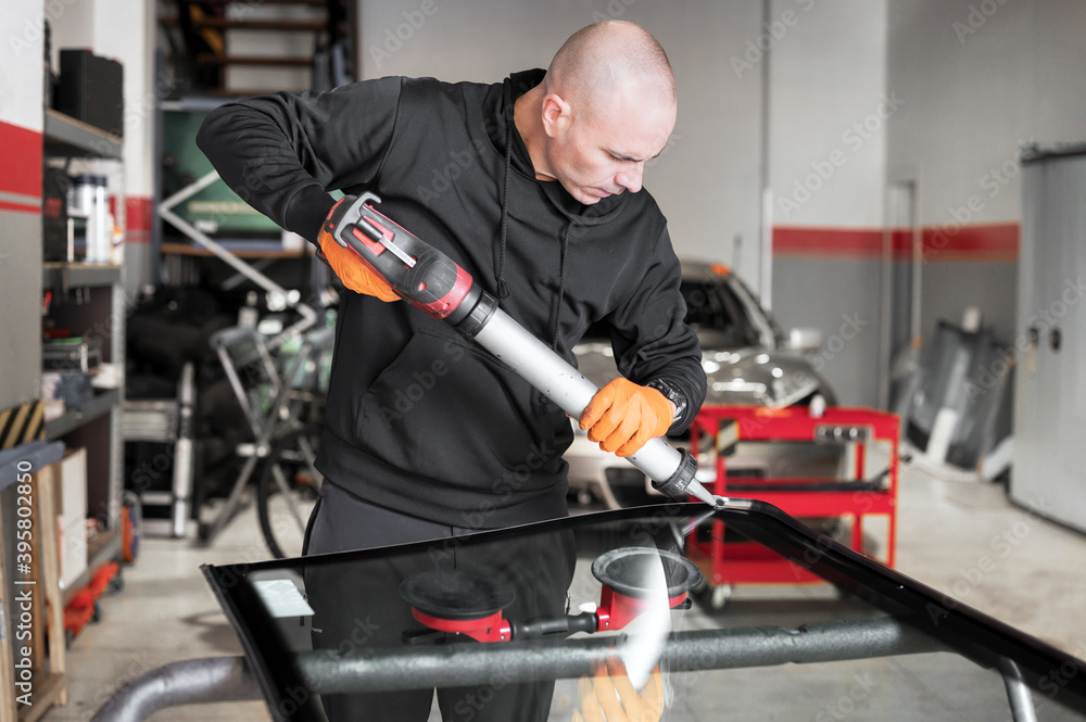 Glazier applying rubber sealing to windshield in garage, close up. High quality photo Glazier applying rubber sealing to windshield in garage, close up. High quality photo