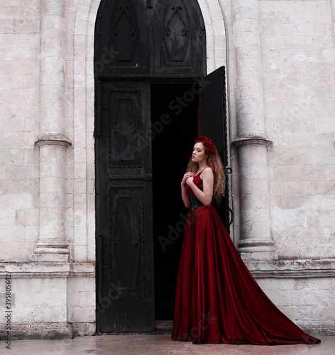 Girl in long red dress standing near church's black door © Альбина Хусаинова