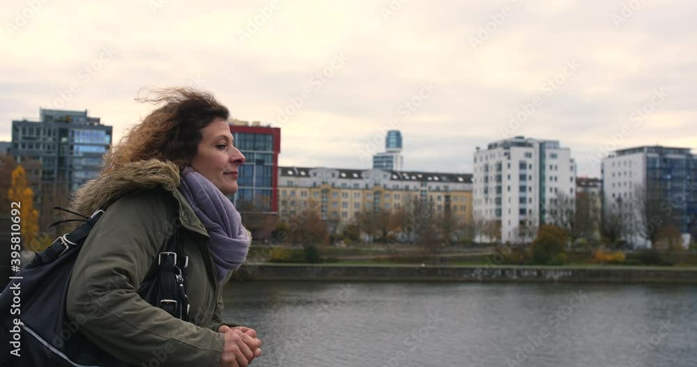 Woman stops at a wall, smiles and waves her hand to a not visible person, may be a friend. The river Main fro Frankfurt is ion the background. Woman stops at a wall, smiles and waves her hand to a not visible person, may be a friend. The river Main fro Frankfurt is ion the background.