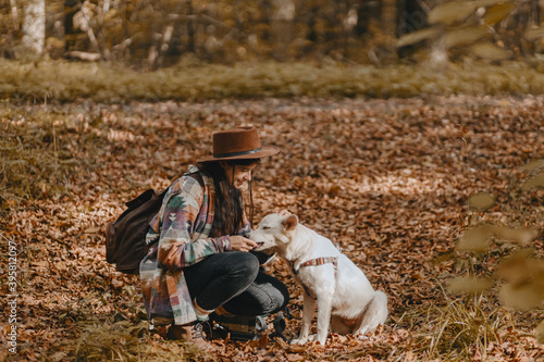 Stylish woman walking with adorable white dog in sunny autumn woods. Cute swiss shepherd puppy