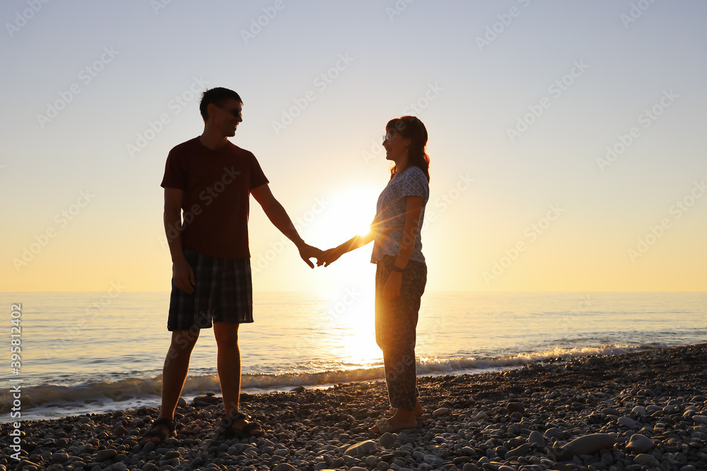 Lovers smile and look at each other in the rays of the setting sun on the seashore. Happy relationship together