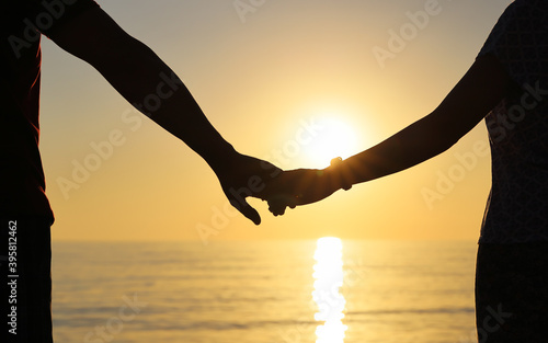 Silhouette of couple holding hands against the setting sun. Strong relationship concept