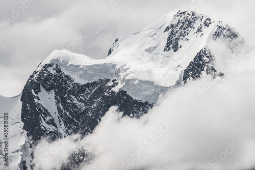 Atmospheric minimalist alpine landscape with massive hanging glacier on snowy mountain peak. Big balcony serac on glacial edge. Low clouds among snowbound mountains. Majestic scenery on high altitude.