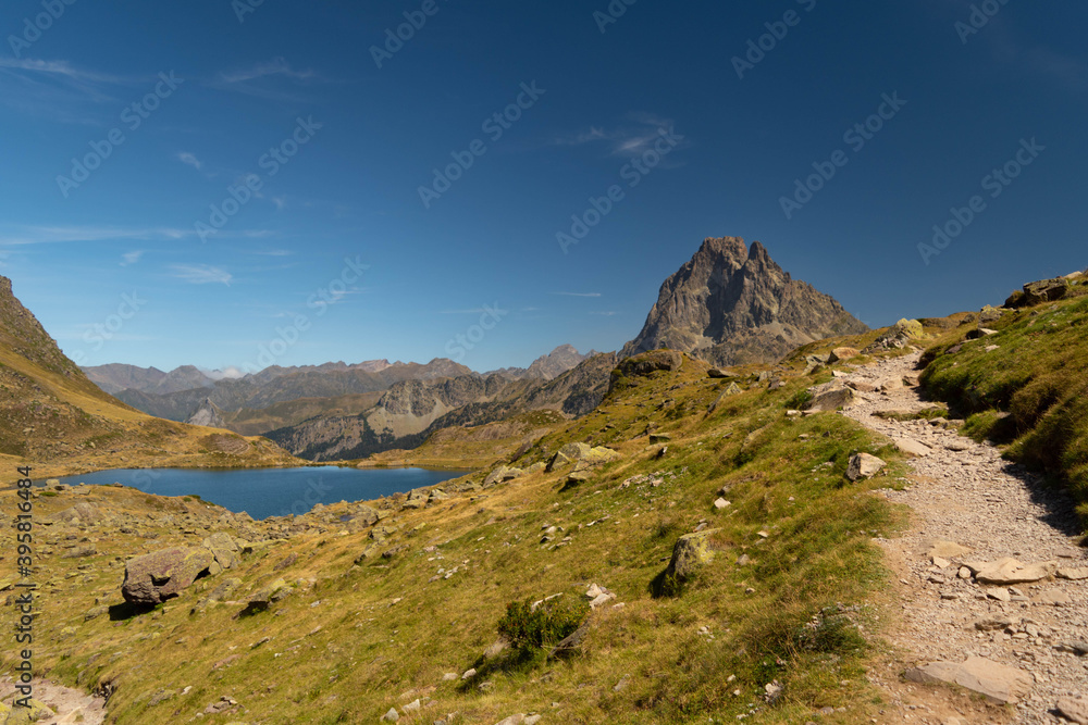 Mountain path with a lake and the Midi d'Ossau peak in the background surrounded by mountains and nature