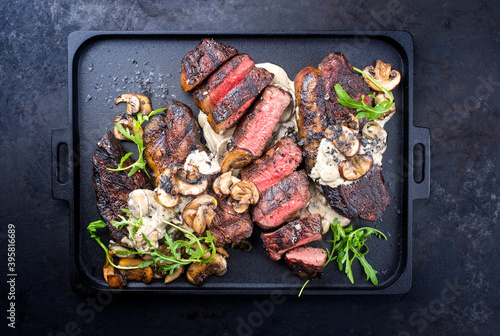 Modern style barbecue dry aged wagyu Brazilian picanha steaks from the sirloin cap of rump beef sliced and served cream sauce and mushrooms as top view on a design tray
