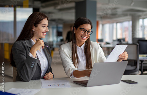 Two successful women are working on a laptop in the office.