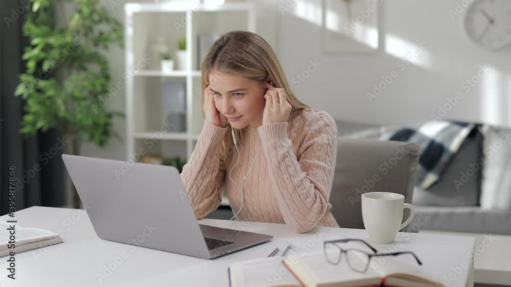 Focused female student in earphones using wireless laptop while studying at home. Concept of remote education and elearning. Focused female student in earphones using wireless laptop while studying at home. Concept of remote education and elearning.
