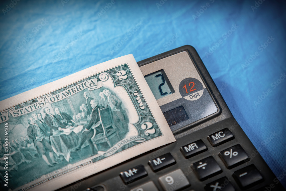 Part of a two dollar American bill and a compact digital calculator on a fabric blue background Part of a two dollar American bill and a compact digital calculator on a fabric blue background