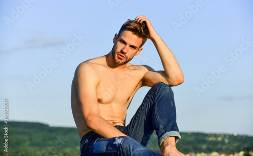 Muscular bare torso. Summer lookbook. Fitness model. Athletic handsome macho wear denim pants. Muscular body. Six packs muscular chest. Man outdoors blue sky background. Male beauty concept