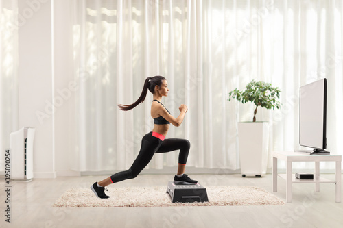 Young female exercising step aerobic in front of tv at home