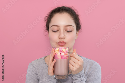 The girl drinks cocoa with marshmallows on a pink background.