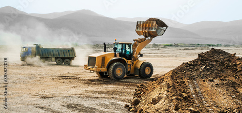 Earthworks on a summer day in a mountainous area. Wheel loaders, bulldozers and dump trucks are in operation. Dust from dump trucks that transport this soil