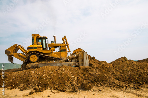Bulldozer at a construction site shovels mountain soil into a heap.