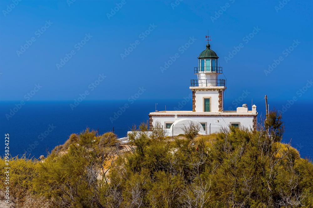 A view past trees towards the lighthouse at Akortiri in Santorini in summertime