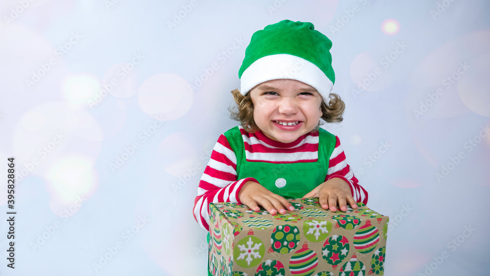 Little elf with a cute smile is sitting on the white background and playing or packing Christmas presents. Christmas holiday background photo.