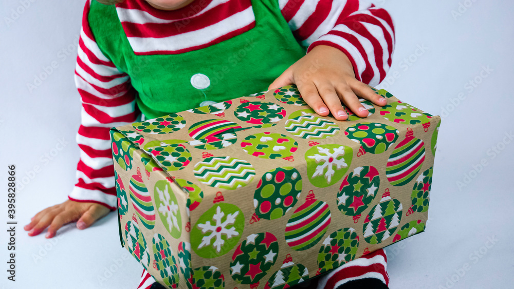 Little elf with a cute smile is sitting on the white background and playing or packing Christmas presents. Christmas holiday background photo.