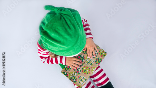 Little elf with a cute smile is sitting on the white background and playing or packing Christmas presents. Christmas holiday background photo.