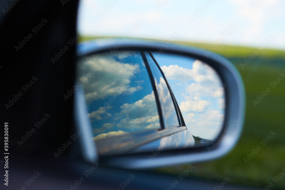 blurred action from car at high speed. Rear view mirror reflecting sky with clouds