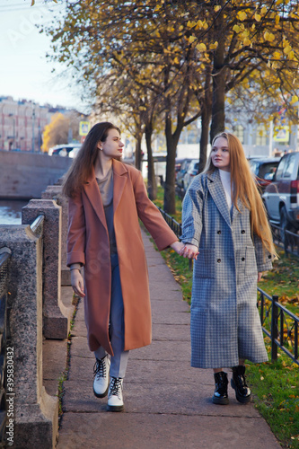 Two fashionable young beautiful stylish woman in coat walking on street. Autumn fashion trend for smiling, happy, purposeful women. Concept style, fashion, beauty and achievement goals. Copy space